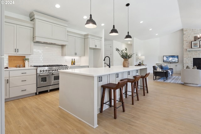 kitchen with hanging light fixtures, light hardwood / wood-style flooring, backsplash, an island with sink, and double oven range