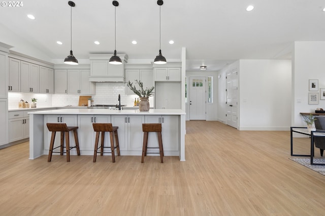 kitchen featuring hanging light fixtures, light wood-type flooring, an island with sink, and a breakfast bar area