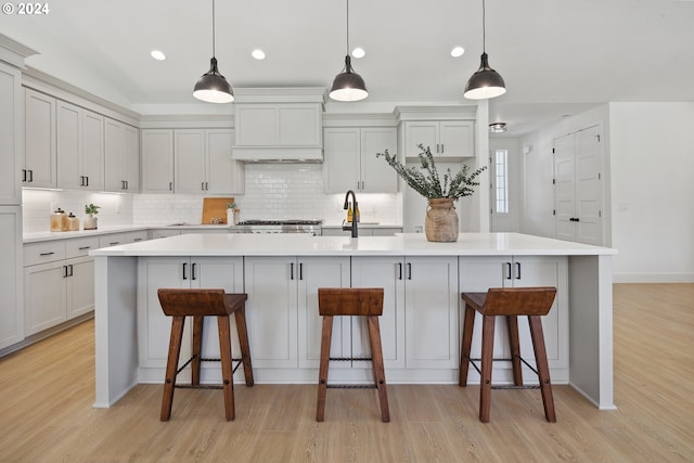 kitchen featuring a large island with sink, premium range hood, and pendant lighting