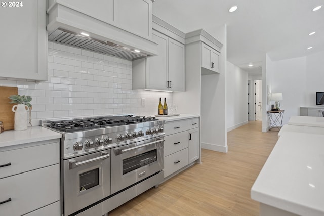 kitchen featuring white cabinetry, tasteful backsplash, range with two ovens, custom exhaust hood, and light wood-type flooring