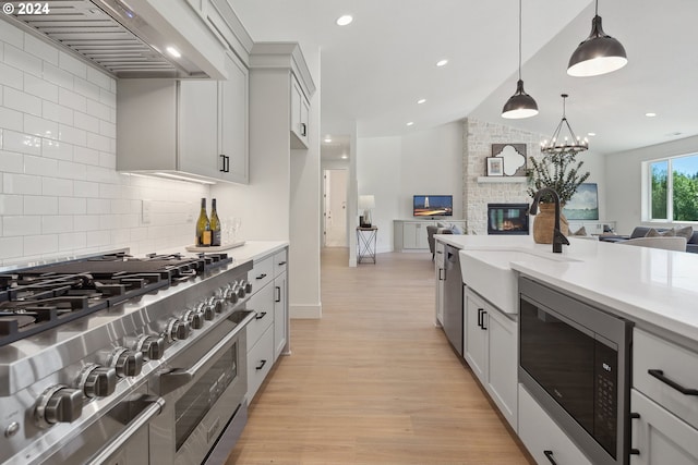 kitchen featuring premium range hood, decorative light fixtures, a fireplace, appliances with stainless steel finishes, and light wood-type flooring