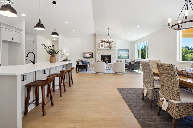 dining area with a stone fireplace, light hardwood / wood-style flooring, a healthy amount of sunlight, and vaulted ceiling