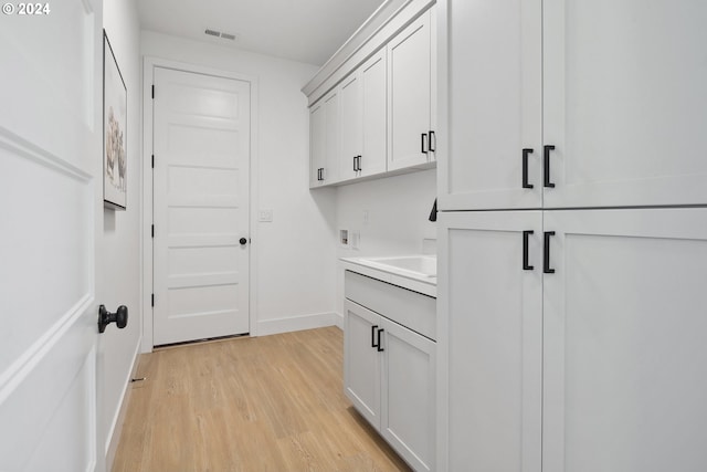 laundry room with cabinets, hookup for a washing machine, light hardwood / wood-style floors, and sink