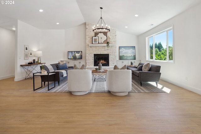 living room featuring light hardwood / wood-style floors, a stone fireplace, lofted ceiling, and an inviting chandelier