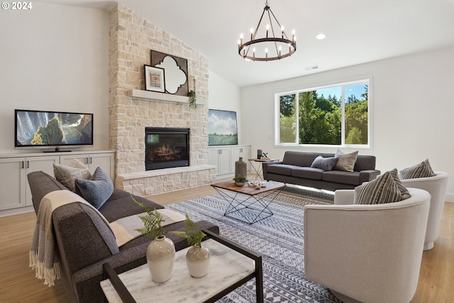 living room with a stone fireplace, an inviting chandelier, vaulted ceiling, and light wood-type flooring