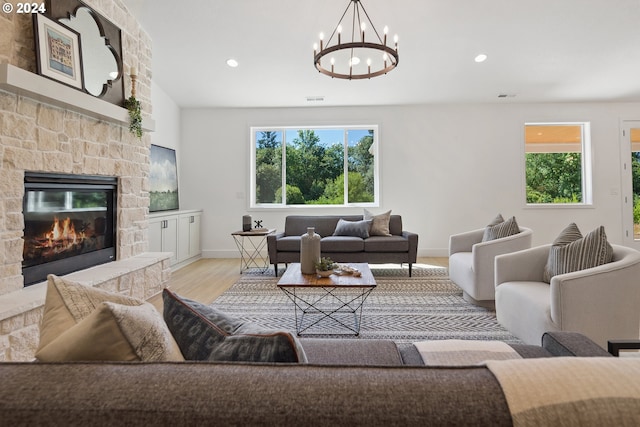 living room featuring a chandelier, light wood-type flooring, and a stone fireplace