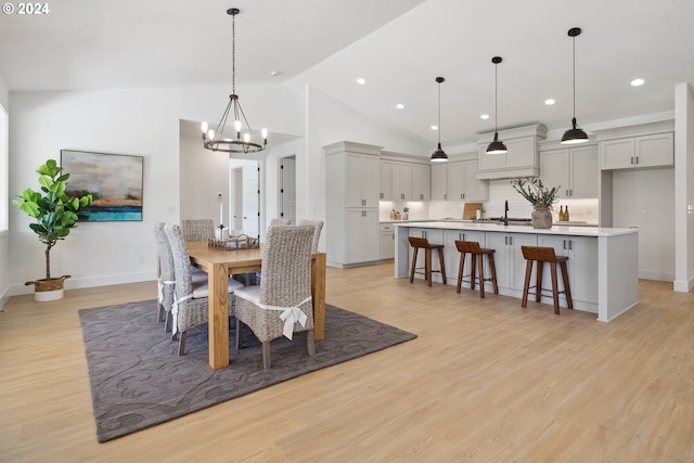 dining room with vaulted ceiling, light hardwood / wood-style floors, an inviting chandelier, and sink