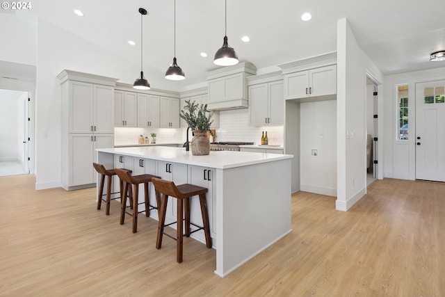 kitchen featuring a large island, backsplash, decorative light fixtures, a breakfast bar, and light wood-type flooring