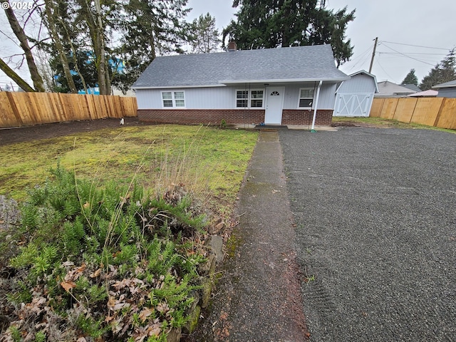 view of front of property featuring a shingled roof, brick siding, fence, and aphalt driveway