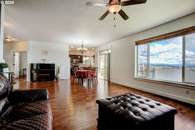 living room with a textured ceiling, ceiling fan with notable chandelier, and dark wood-type flooring