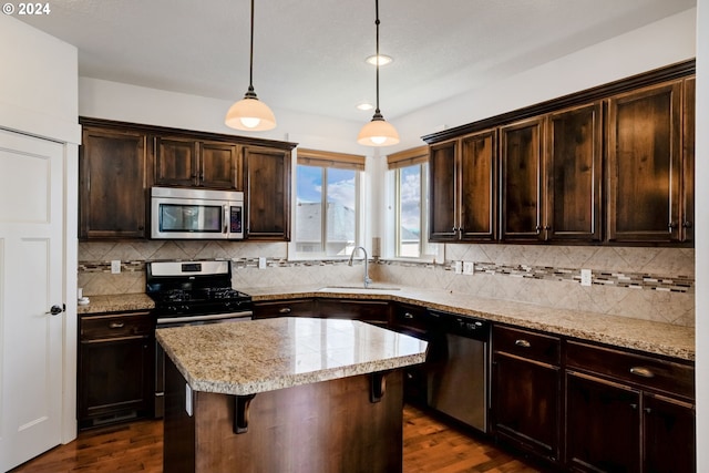 kitchen featuring a kitchen island, stainless steel appliances, decorative light fixtures, dark hardwood / wood-style flooring, and sink