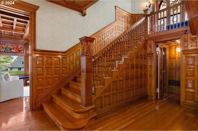 staircase with coffered ceiling, beamed ceiling, and hardwood / wood-style floors