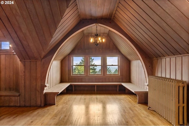 additional living space featuring vaulted ceiling, an inviting chandelier, light hardwood / wood-style flooring, radiator, and wood walls