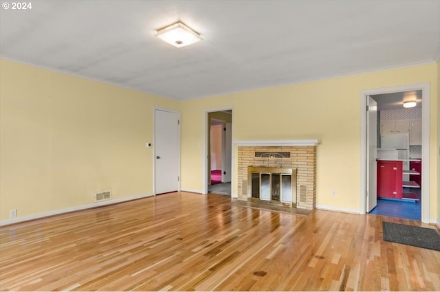 unfurnished living room featuring baseboards, visible vents, crown molding, light wood-type flooring, and a brick fireplace