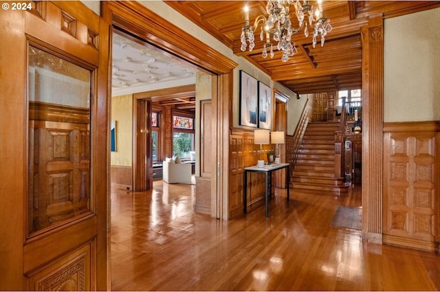 hallway with a wainscoted wall, ornamental molding, wood finished floors, wooden ceiling, and stairs