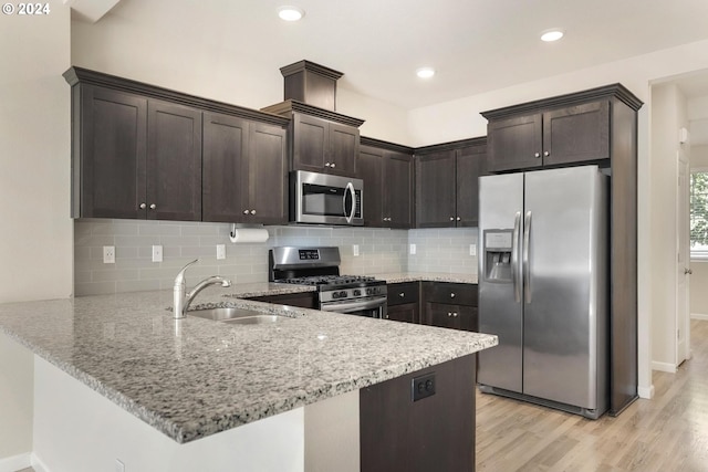 kitchen with dark brown cabinets, sink, kitchen peninsula, light hardwood / wood-style flooring, and appliances with stainless steel finishes