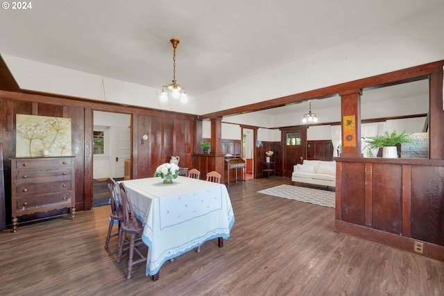 dining area featuring decorative columns, wood walls, and dark wood-type flooring