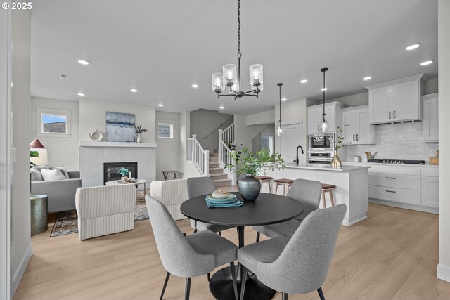 12785 SW Trask St, Beaverton, OR 97007 - dining area featuring light wood-style flooring, recessed lighting, a tile fireplace, stairs, and a chandelier