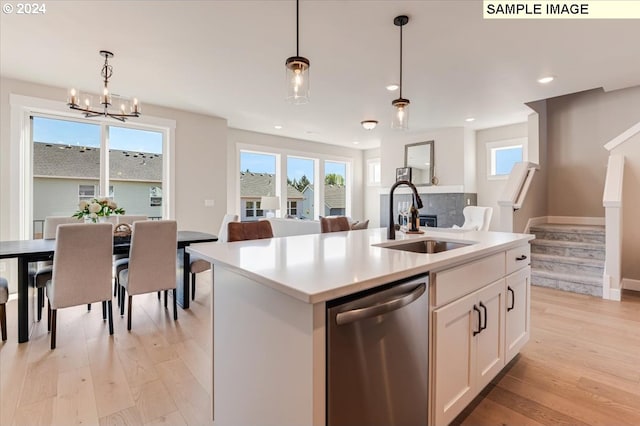 kitchen featuring pendant lighting, a kitchen island with sink, sink, stainless steel dishwasher, and white cabinetry