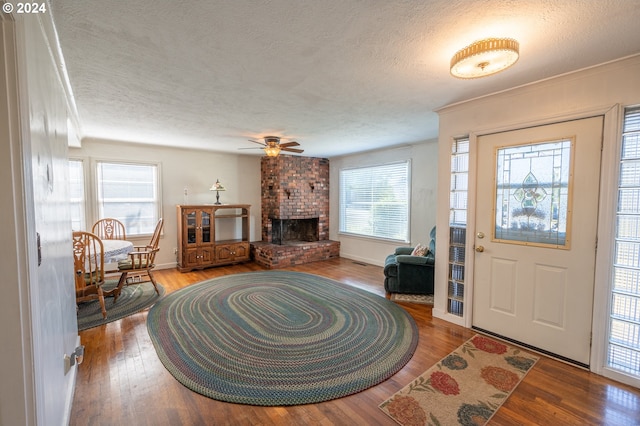 foyer featuring a brick fireplace, a textured ceiling, wood-type flooring, crown molding, and ceiling fan