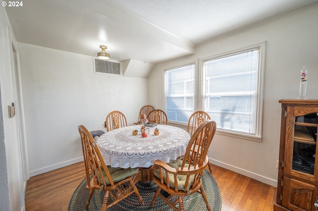 dining room with light hardwood / wood-style flooring, ornamental molding, vaulted ceiling, and a healthy amount of sunlight