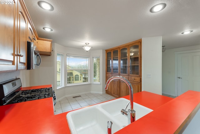 kitchen with gas range, sink, light tile patterned floors, and a textured ceiling