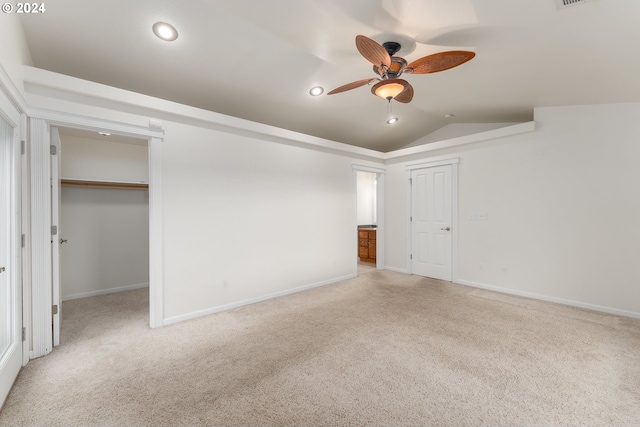 unfurnished bedroom featuring lofted ceiling, light carpet, a walk in closet, ceiling fan, and a closet