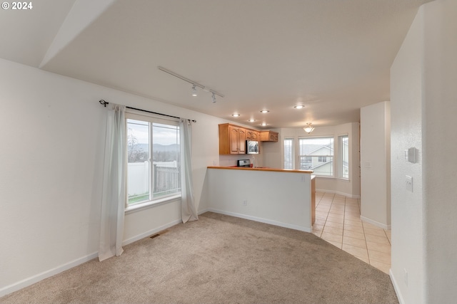 unfurnished living room with rail lighting, a healthy amount of sunlight, and light carpet