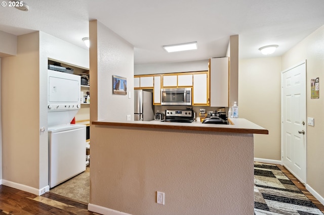 kitchen with kitchen peninsula, light hardwood / wood-style flooring, stacked washer / dryer, and appliances with stainless steel finishes