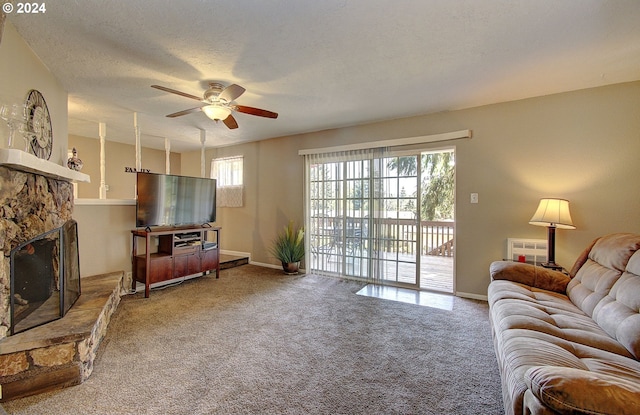 carpeted living room with ceiling fan, a wealth of natural light, a textured ceiling, and a stone fireplace