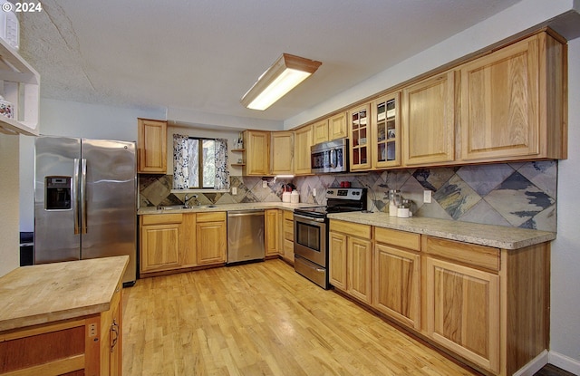 kitchen with stainless steel appliances, light stone countertops, sink, light hardwood / wood-style flooring, and decorative backsplash