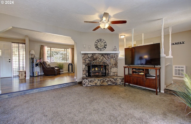 carpeted living room featuring ceiling fan, a textured ceiling, and a stone fireplace