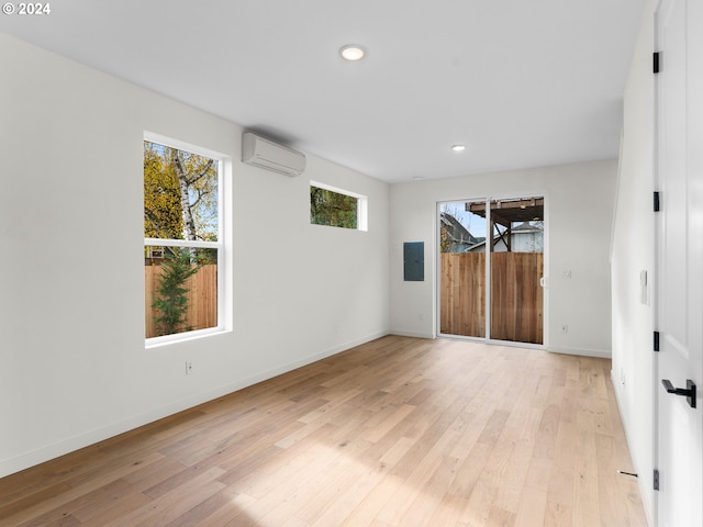 spare room with plenty of natural light, light hardwood / wood-style floors, an AC wall unit, and electric panel