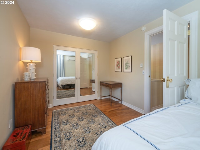 bedroom featuring wood finished floors, baseboards, french doors, a closet, and a wall mounted AC