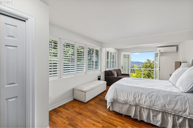 bedroom with wood finished floors, baseboards, and a wall mounted AC