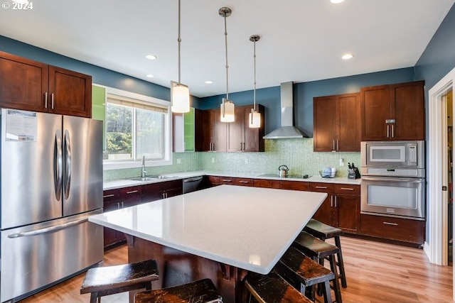 kitchen with wall chimney exhaust hood, a kitchen island, appliances with stainless steel finishes, and a kitchen bar