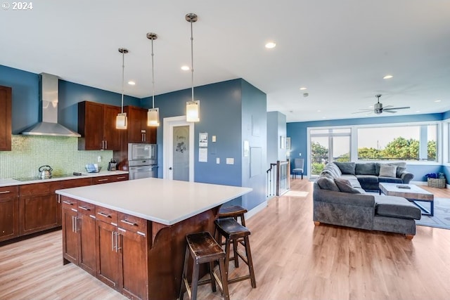 kitchen with oven, wall chimney range hood, a kitchen bar, light wood-type flooring, and a kitchen island