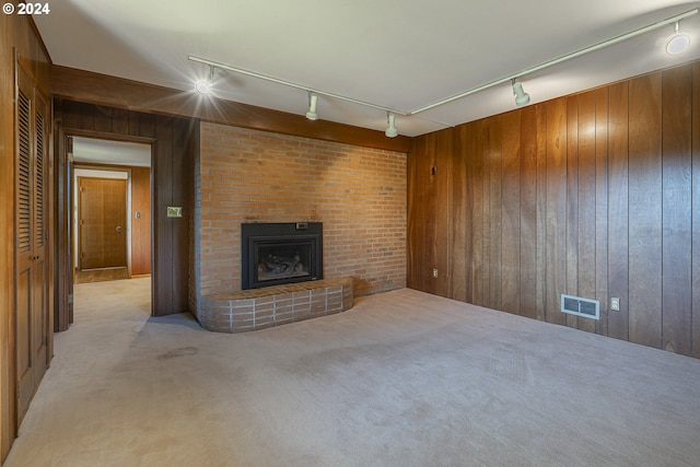 unfurnished living room with light colored carpet, rail lighting, a brick fireplace, and wood walls