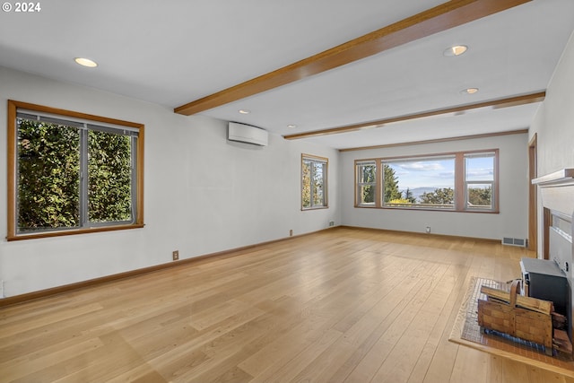 unfurnished living room featuring beamed ceiling, a wall mounted AC, and light wood-type flooring