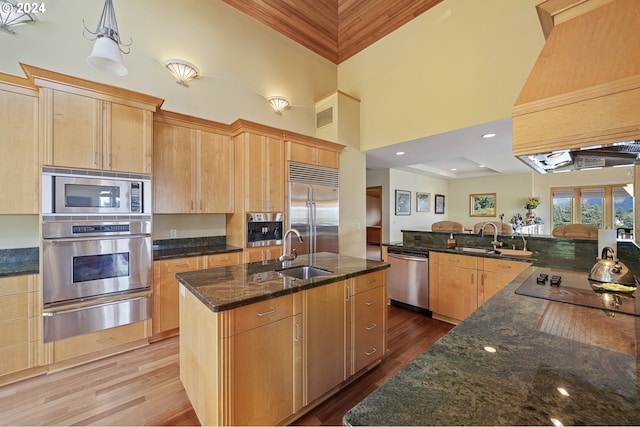 kitchen featuring a towering ceiling, sink, built in appliances, a center island with sink, and hardwood / wood-style flooring