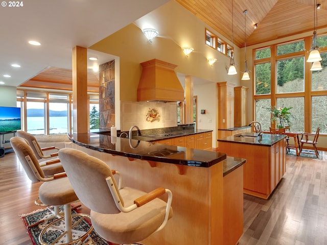 kitchen with kitchen peninsula, pendant lighting, a breakfast bar area, wood ceiling, and custom range hood