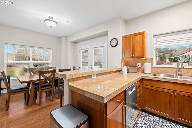 kitchen with kitchen peninsula, sink, stainless steel dishwasher, and light hardwood / wood-style floors