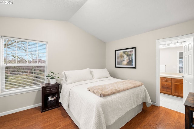 bedroom featuring connected bathroom, hardwood / wood-style floors, multiple windows, and vaulted ceiling