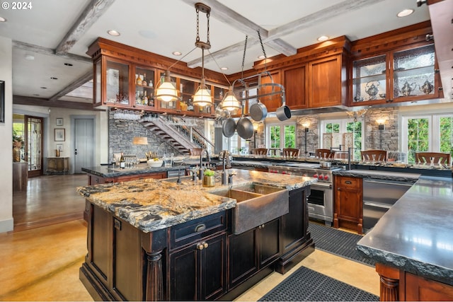 kitchen featuring hanging light fixtures, sink, a center island with sink, stainless steel stove, and dark stone countertops