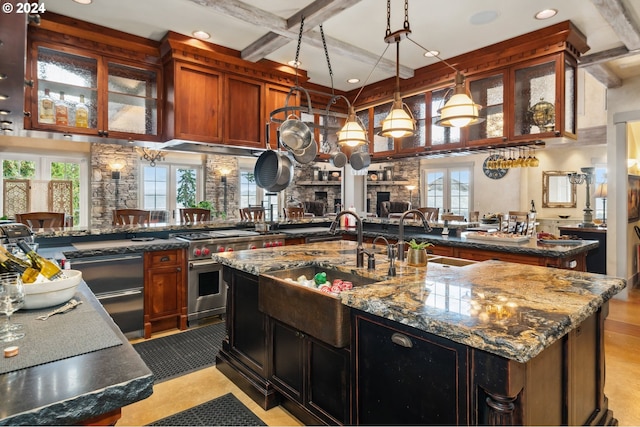 kitchen featuring high end stainless steel range, light stone countertops, a kitchen island with sink, and kitchen peninsula