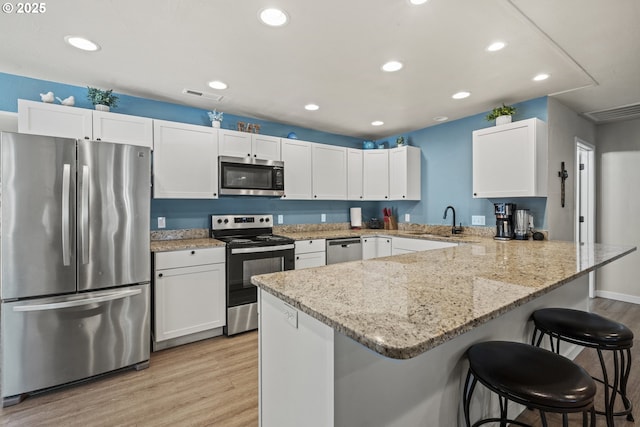 kitchen with white cabinetry, stainless steel appliances, light stone counters, a breakfast bar, and light hardwood / wood-style flooring