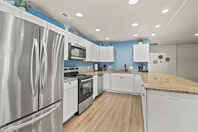 kitchen with white cabinets, stainless steel appliances, sink, light wood-type flooring, and light stone counters