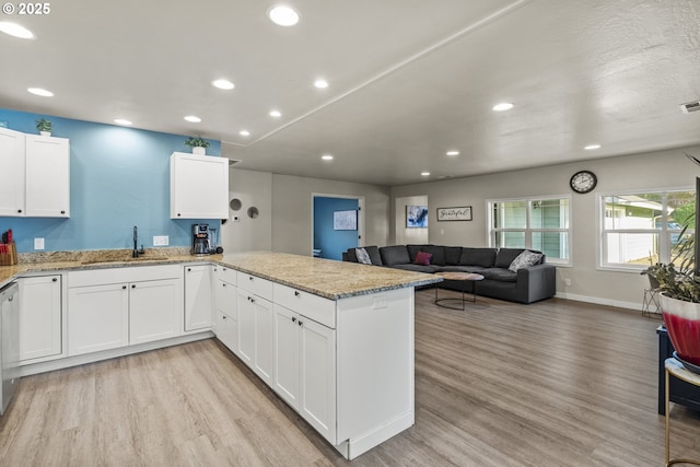 kitchen with kitchen peninsula, white cabinets, sink, and light hardwood / wood-style floors