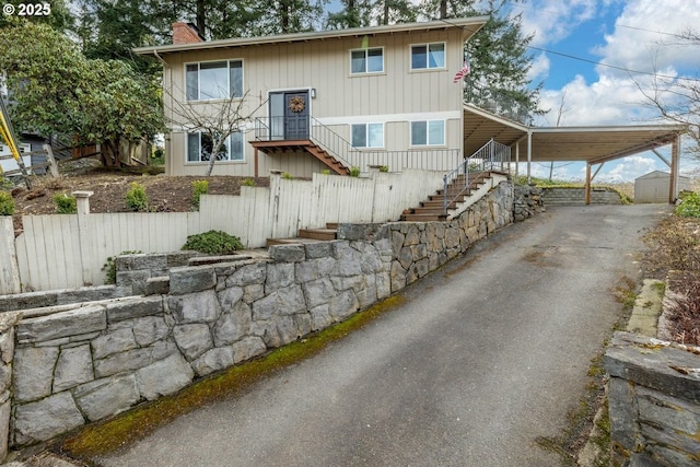 raised ranch featuring driveway, stairway, an attached carport, a chimney, and fence