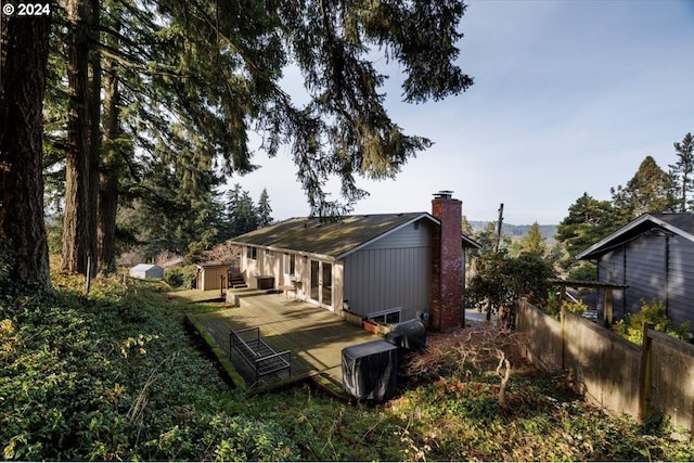 rear view of house with fence, a deck, and a chimney